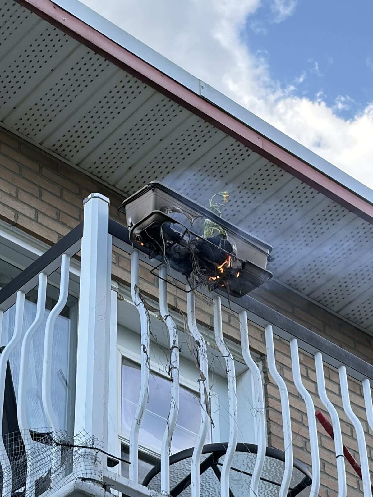 A small fire burning in a planter hanging from a balcony.